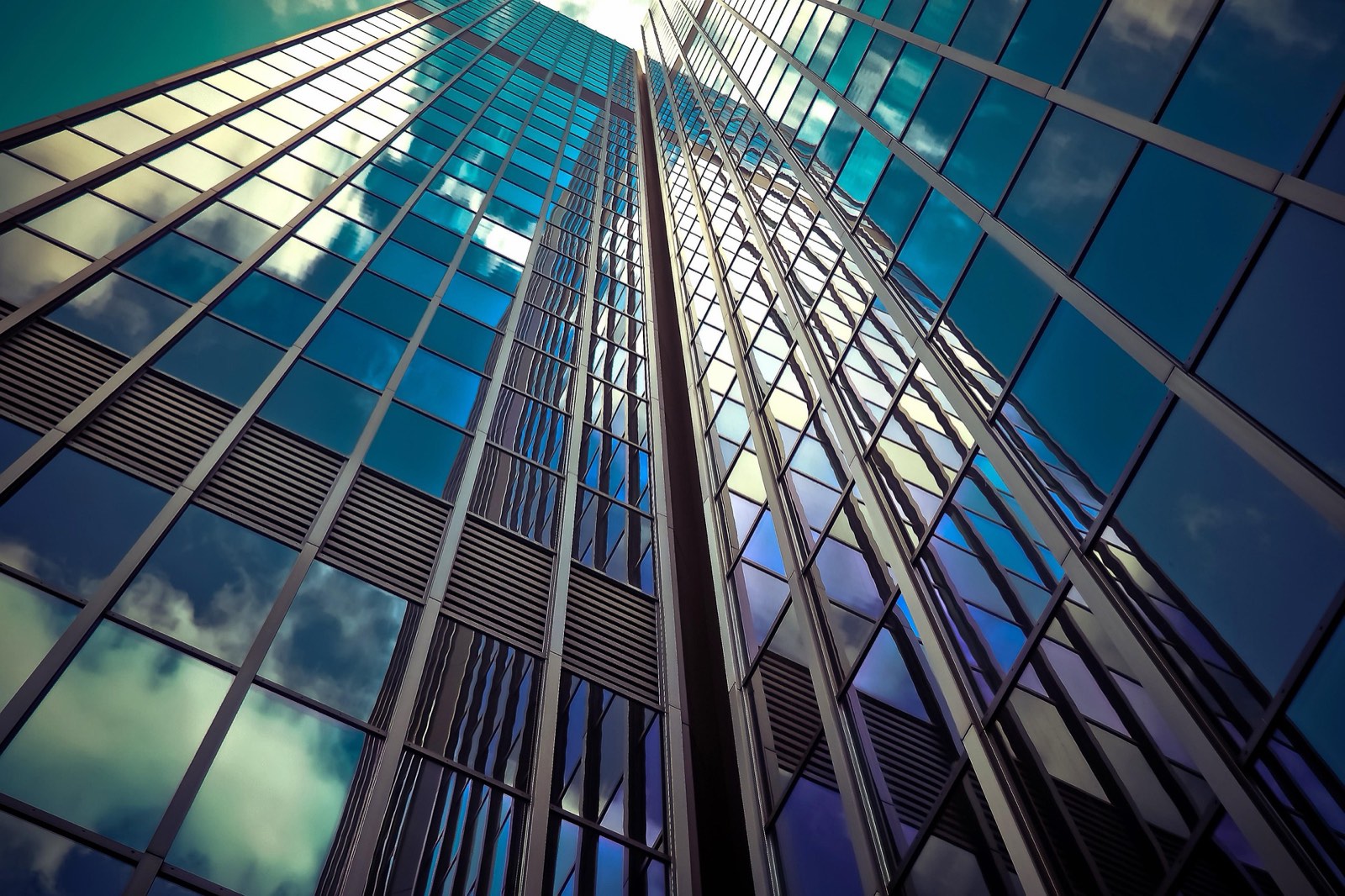 A glass curtain wall seen from below, reflecting sky and cloud.