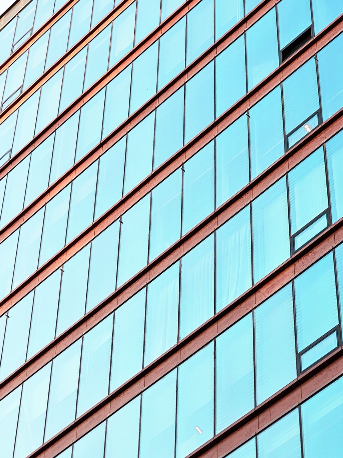 La façade d'un immeuble en panneaux vitrés bleu pâle disposés en trame régulière, séparés par des bandeaux horizontaux de teinte chaude.